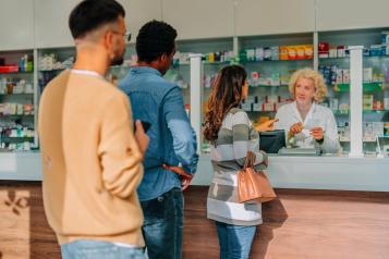 A couple of diverse people are standing in the queue at the pharmacy, waiting for their turn.