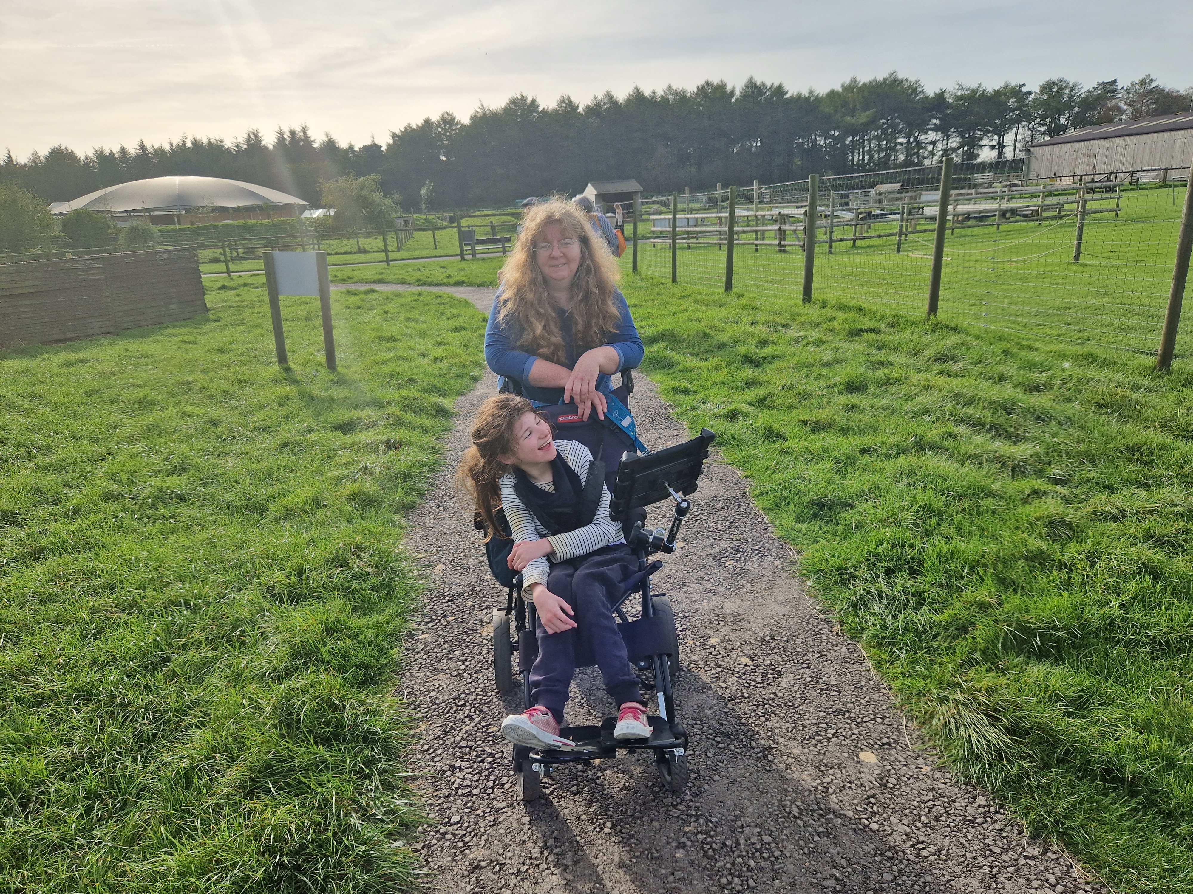 Lorna pushes her daughter on a path through two fields. The sun is setting in the background.