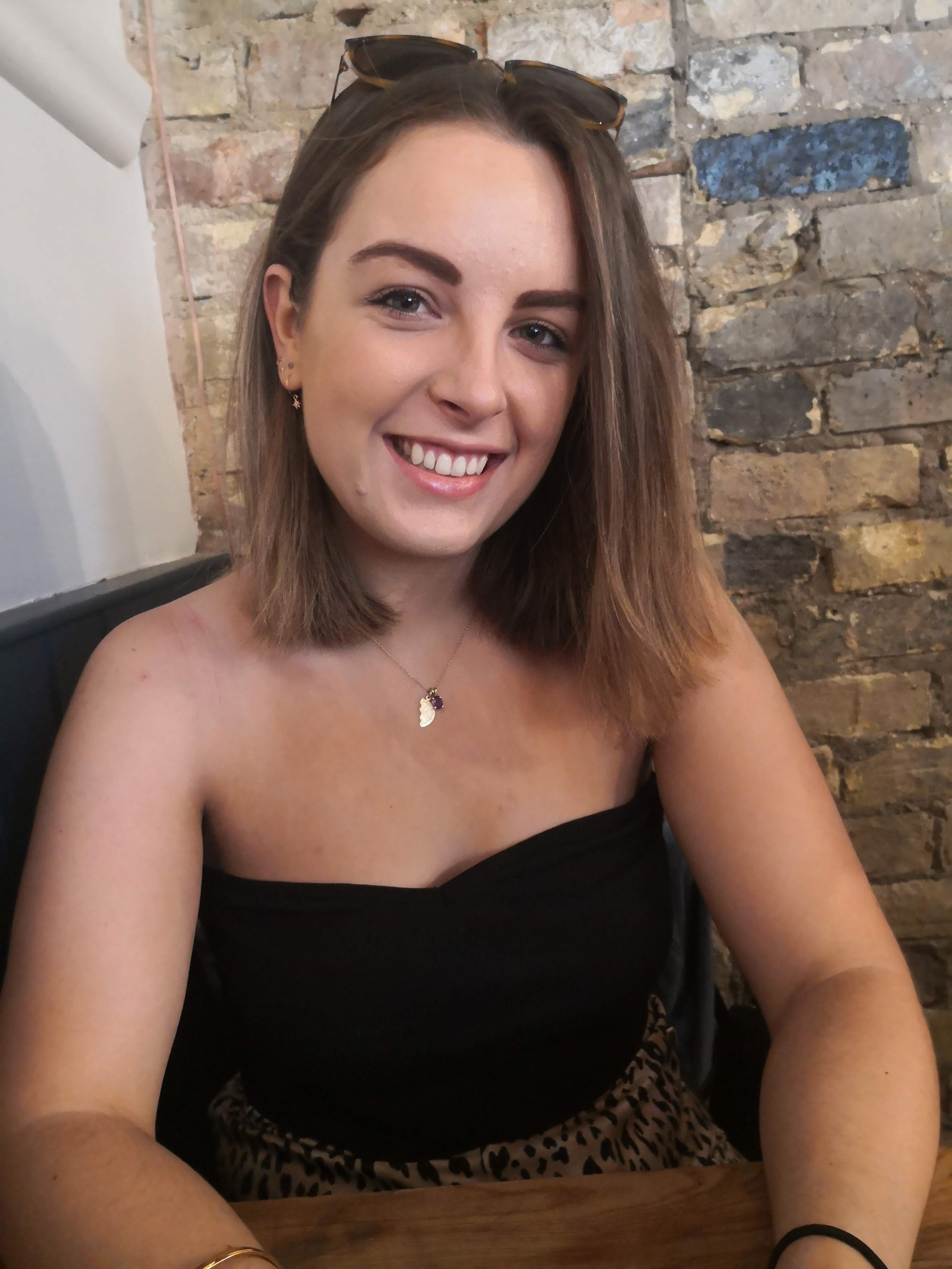 A picture of a white woman, 29, wearing a black top and sitting in a cafe.