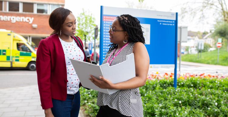 A Healthwatch volunteer with a clipboard speaking to a woman outside a hospital