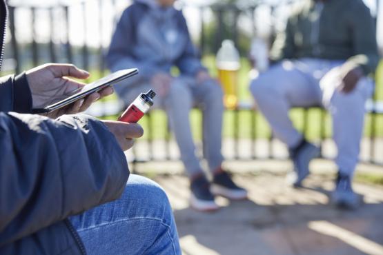 Close Up Of Teenagers With Mobile Phone Vaping in a park