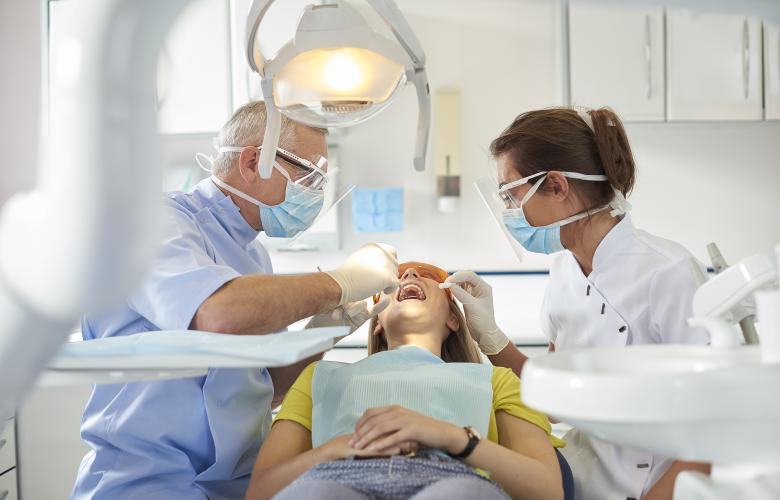 A dentist and dental nurse sit either side of a young woman as they carry out an exam in a bright surgery space